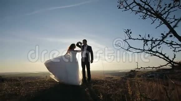 新娘在日落时分在山岩上的新郎附近旋转视频的预览图