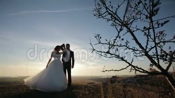 新娘在日落时分在山岩上的新郎附近旋转视频的预览图