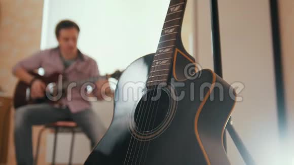 年轻迷人的音乐家用吉他和戏剧作曲前景中的其他乐器模糊视频的预览图