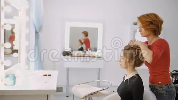 豪华美容院的女理发师正在与年轻的金发模特站在一起工作视频的预览图