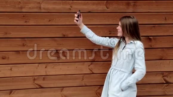 快乐的白种人少女在手机木制背景上自拍视频的预览图