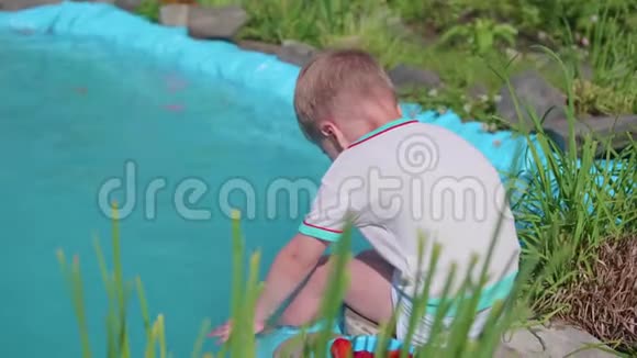 那个男孩坐在一个小湖边这孩子用脚造成水溅夏日炎炎快乐的童年视频的预览图