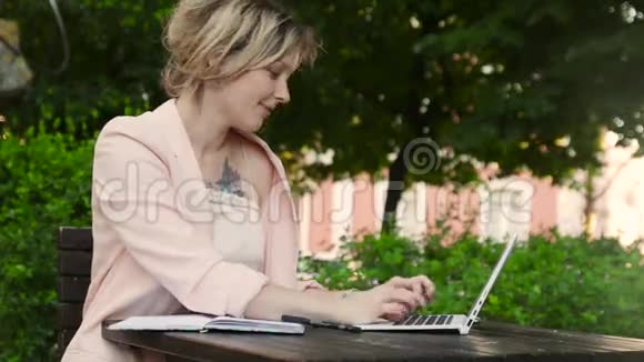 阳光明媚的一天漂亮的金发白女在公园里自由工作手提电脑和智能手机视频的预览图
