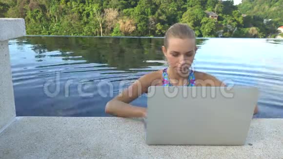 户外照片美丽的金发美女穿着比基尼带着笔记本电脑在屋顶无限的游泳池里视频的预览图
