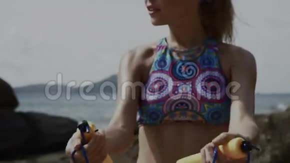 夏天一个漂亮的金发女人在海边的岩石之间用跳绳视频的预览图