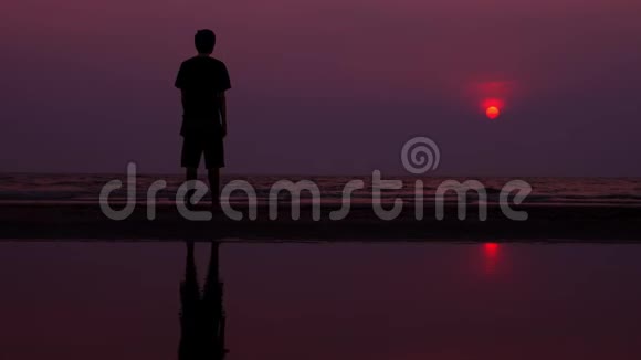剪影夕阳下孤独的亚洲年轻人平静地沿着一片荒芜的海滩散步海景视频的预览图