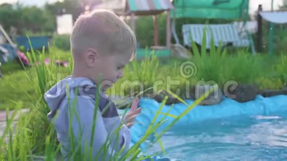 那个男孩坐在一个小湖边这孩子用脚造成水溅夏日炎炎快乐的童年视频的预览图