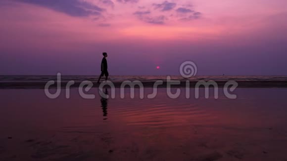 剪影孤独的亚洲年轻人在日落时平静地沿着一片荒芜的海滩散步海景视频的预览图