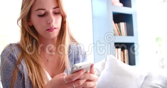 使用移动电话在家庭办公室里坐着沙发的女人视频的预览图