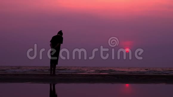 剪影孤独的亚洲年轻人在日落时平静地沿着一片荒芜的海滩散步海景视频的预览图