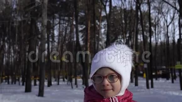 一个戴眼镜的女孩的肖像一顶白色的帽子和一件红色的夹克女孩在镜头前微笑并表现出情感视频的预览图