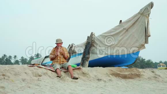 老人在渔船旁边的海滩上吹竹笛视频的预览图