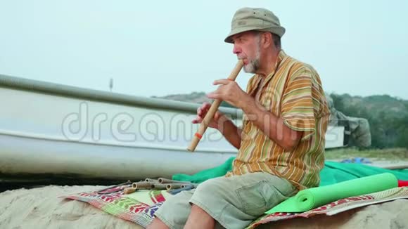 老人在渔船旁边的海滩上吹竹笛视频的预览图