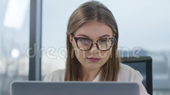 戴眼镜的年轻女士看着笔记本电脑视频的预览图