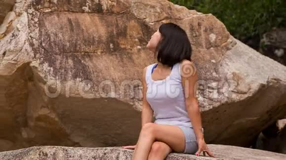 女孩坐在岩石上欣赏石头和山涧的景色视频的预览图