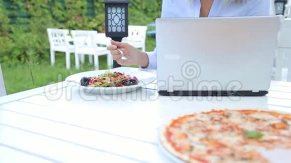 年轻女子用笔记本电脑和沙拉坐在城市的咖啡馆里视频的预览图