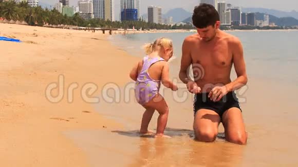 父亲给坐在海边海水边的小女孩喂奶视频的预览图