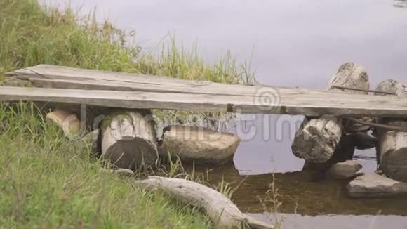 从平静的河流中建造的原木和石头制成的自制木桥视频的预览图