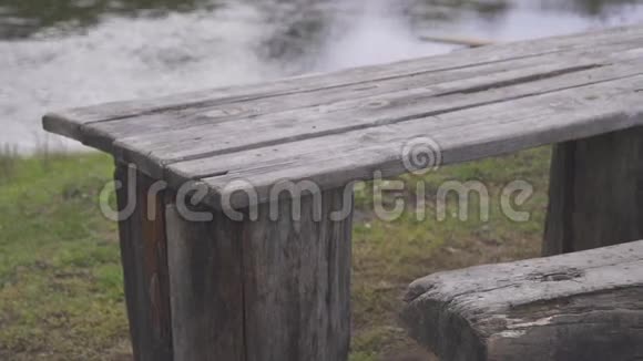 在河边的绿色草地上旧的木制桌子和长凳视频的预览图