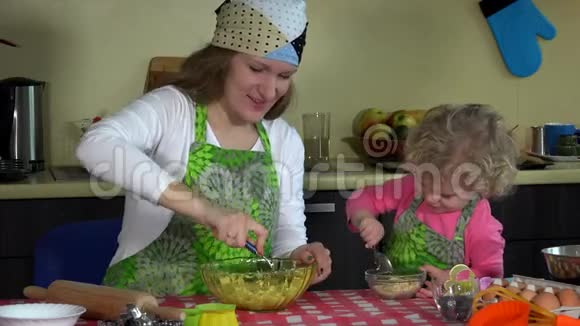 快乐的母亲和穿着围裙的小女儿一起烘焙厨房里的家庭女孩视频的预览图