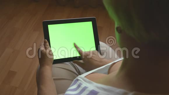 老年妇女坐在家里的沙发上使用带有绿色屏幕的数字平板电脑后视成人平板电脑视频的预览图
