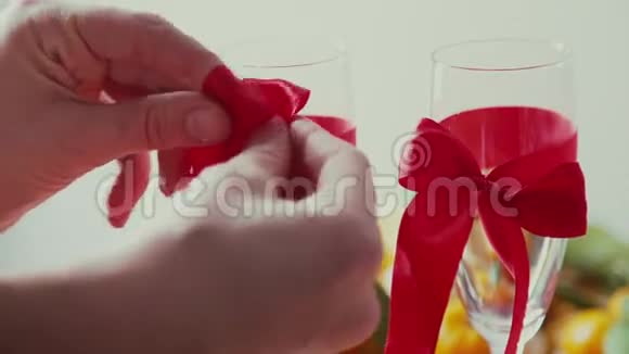 双手把红蝴蝶结绑在透明的香槟杯上视频的预览图