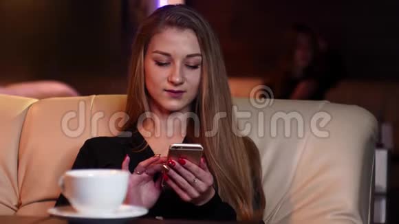 金发女孩喝着咖啡在电话里聊天慢动作地坐在4k分辨率的米色沙发上视频的预览图