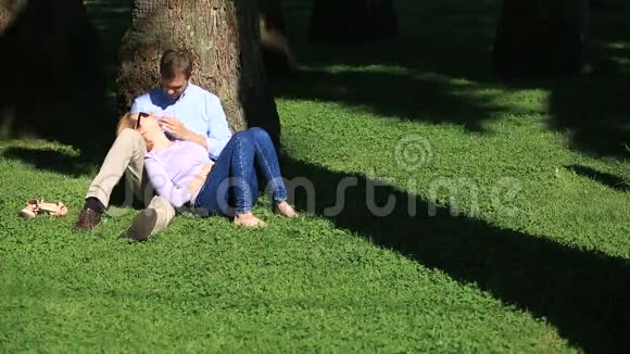 一对浪漫的情侣坐在棕榈树下一个女孩在一个男人的大腿上一对相爱的夫妇在草地上的公园里休息视频的预览图