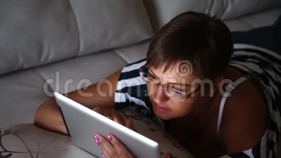 躺在家里沙发上看平板电脑照片的年轻女子视频的预览图