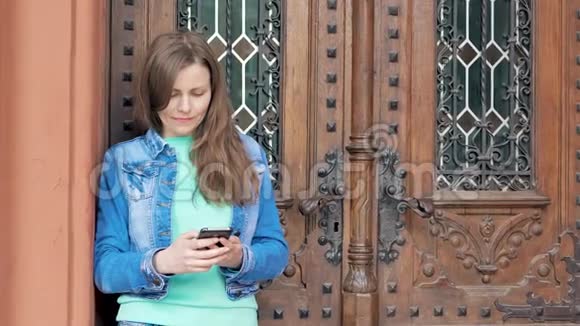 穿着棉袄用智能手机的漂亮女孩背景中的老式建筑视频的预览图