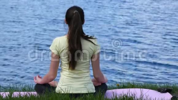 年轻女子在海滩上放松冥想坐在草地上打坐在河边做瑜伽的女孩视频的预览图