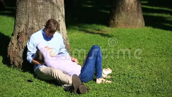 一对浪漫的情侣坐在棕榈树下一个女孩在一个男人的大腿上一对相爱的夫妇在草地上的公园里休息视频的预览图