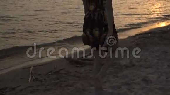 美丽的女孩穿着轻盈的裙子在夕阳下漫步在海滩上微笑着视频的预览图