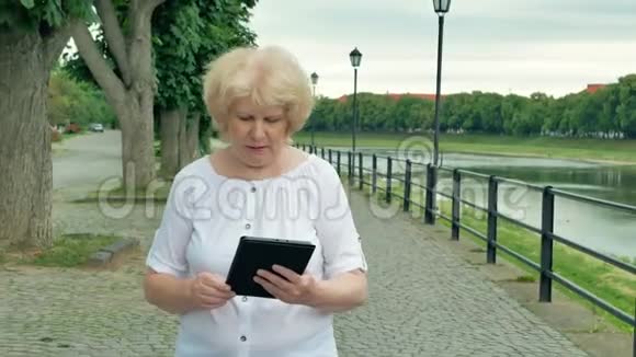 老年妇女沿着海滨散步使用平板电脑河流的背景视频的预览图