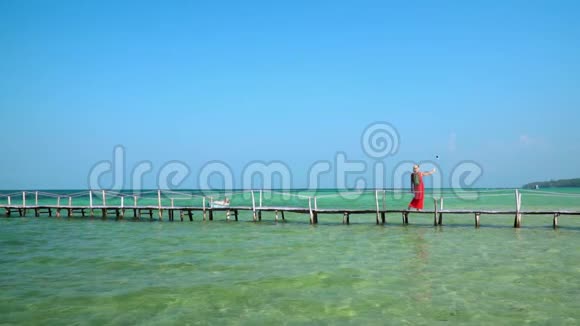 一位漂亮的女士用自拍棒上的动作相机拍摄自己的视频岛上阳光明媚普惠视频的预览图