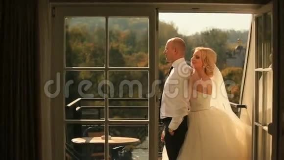 美丽的新娘和英俊的新郎拥抱在阳台上蜜月概念视频的预览图