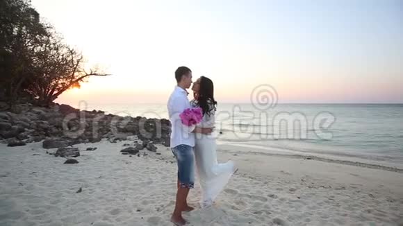 日出时新郎新娘在沙滩拥抱视频的预览图