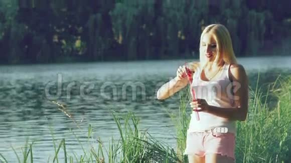 快乐的女孩在湖边的夏季公园吹肥皂泡慢慢地视频的预览图