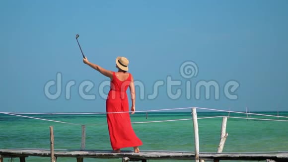 那个女人拿着Selfie棍子走在码头上慢吞吞的穿着红色长裙的女人被拍到视频的预览图