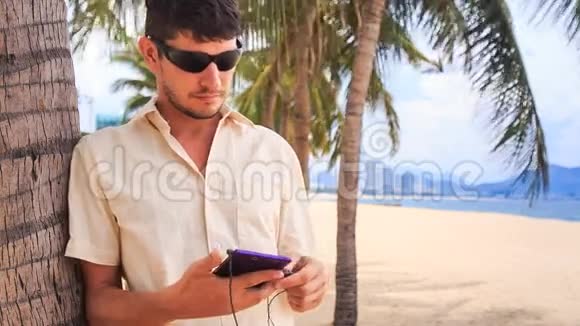 太阳眼镜男在沙滩棕榈树下经营iphone视频的预览图