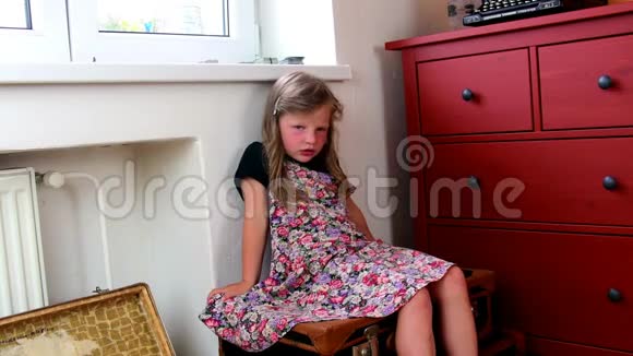 可爱的小女孩坐在老式的手提箱上等待开始度假小女孩穿花裙子旅行视频的预览图