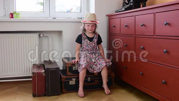 可爱的小女孩坐在老式的手提箱上等待开始度假小女孩穿花裙子旅行视频的预览图