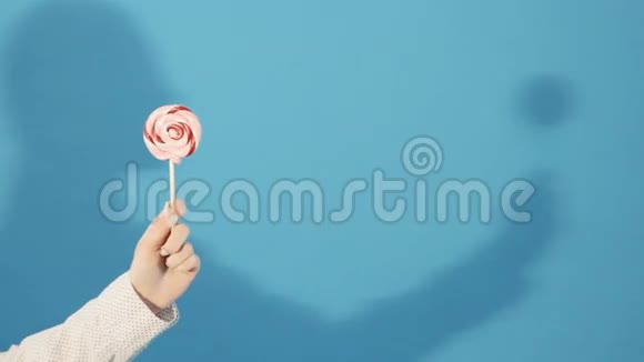 女性手拿着五颜六色的棒棒糖在蓝色背景与女孩阴影在工作室视频的预览图