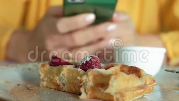 美女正在咖啡馆吃华夫饼用智能手机拍照视频的预览图