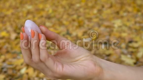 女性手用橙色指甲手拿粉红色石英黄色的鸡蛋以供Vumfit模仿或冥想黄色的跌倒视频的预览图