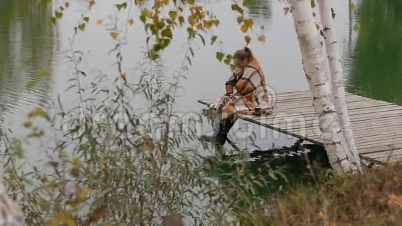 女人坐在柳树下的木凳上在湖边迎风而动视频的预览图