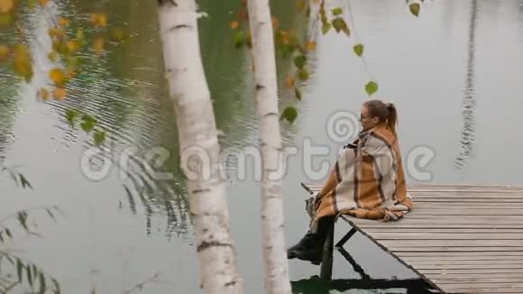 女人坐在柳树下的木凳上在湖边迎风而动视频的预览图