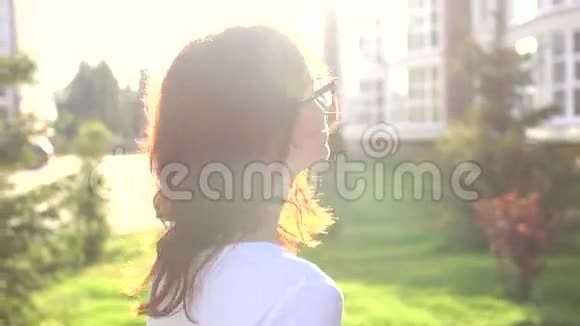视频肖像少女戴着眼镜走在公园里摇头发视频的预览图