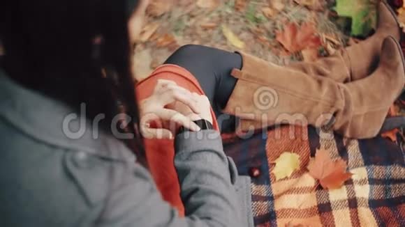 美丽时尚年轻的女士使用智能时钟坐在格子在秋季公园4k视频的预览图