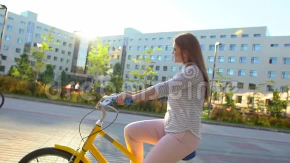 年轻快乐的女人在夏天的户外快乐地骑自行车穿过阳光明媚的街道年轻少女骑着自行车视频的预览图